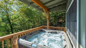 A hot tub on a wooden deck with a view of a forest.