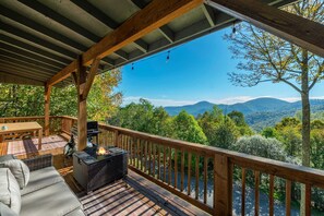 Um deck coberto ao ar livre, com churrasqueira e área de estar, com vista para uma paisagem montanhosa.