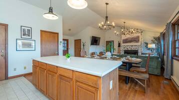 A spacious kitchen with wooden cabinets, a central island, pendant lighting, and a stone fireplace.