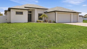 A two-story house with a garage, a front door, and a small garden with a palm tree. - Backyard Oasis Pool Game Room Sleeps 10 (Cape Coral)