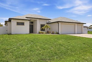 A two-story house with a garage, a front door, and a small garden with a palm tree. - Backyard Oasis Pool Game Room Sleeps 10 (Cape Coral)