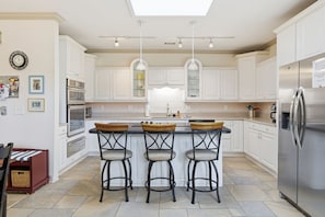 A modern kitchen with white cabinetry, a central island with bar stools, a stainless steel refrigerator, and pendant lighting. - Vacation Paradise - Private Pool Fire Pit BBQ (Hilton Head Island)