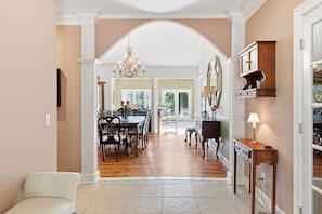 A spacious living area with a dining table, chairs, and a chandelier. There is a white sofa and a wooden cabinet with a lamp. - Vacation Paradise - Private Pool Fire Pit BBQ (Hilton Head Island)