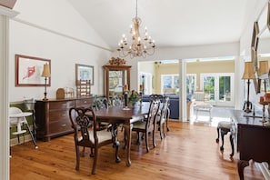 A dining area with a wooden table and chairs, a chandelier, and a view through a glass door to an outdoor space. - Vacation Paradise - Private Pool Fire Pit BBQ (Hilton Head Island)