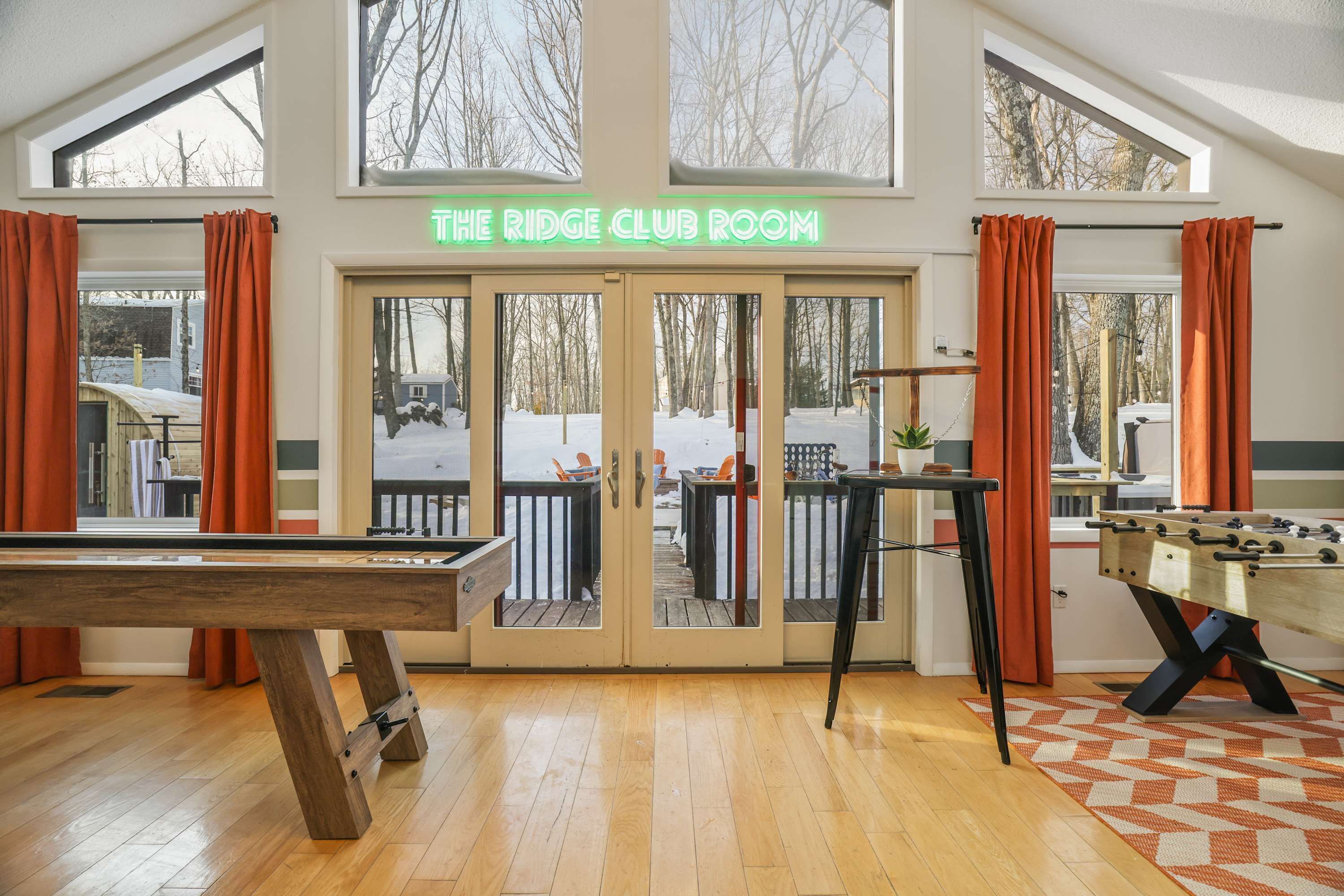 A room with a pool table, foosball table, and a view of a snowy deck outside.