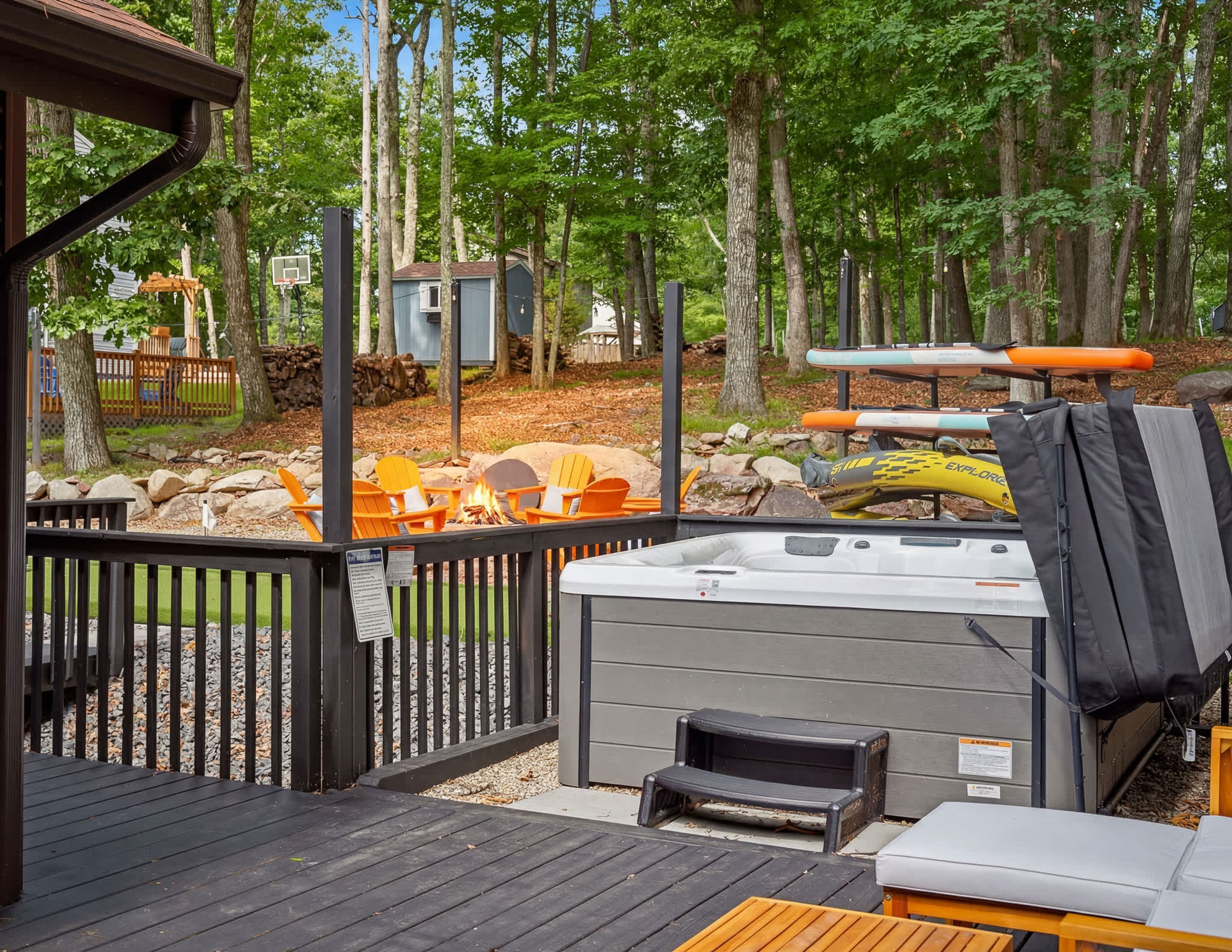 A deck with a hot tub, outdoor seating, and a view of the surrounding wooded area.