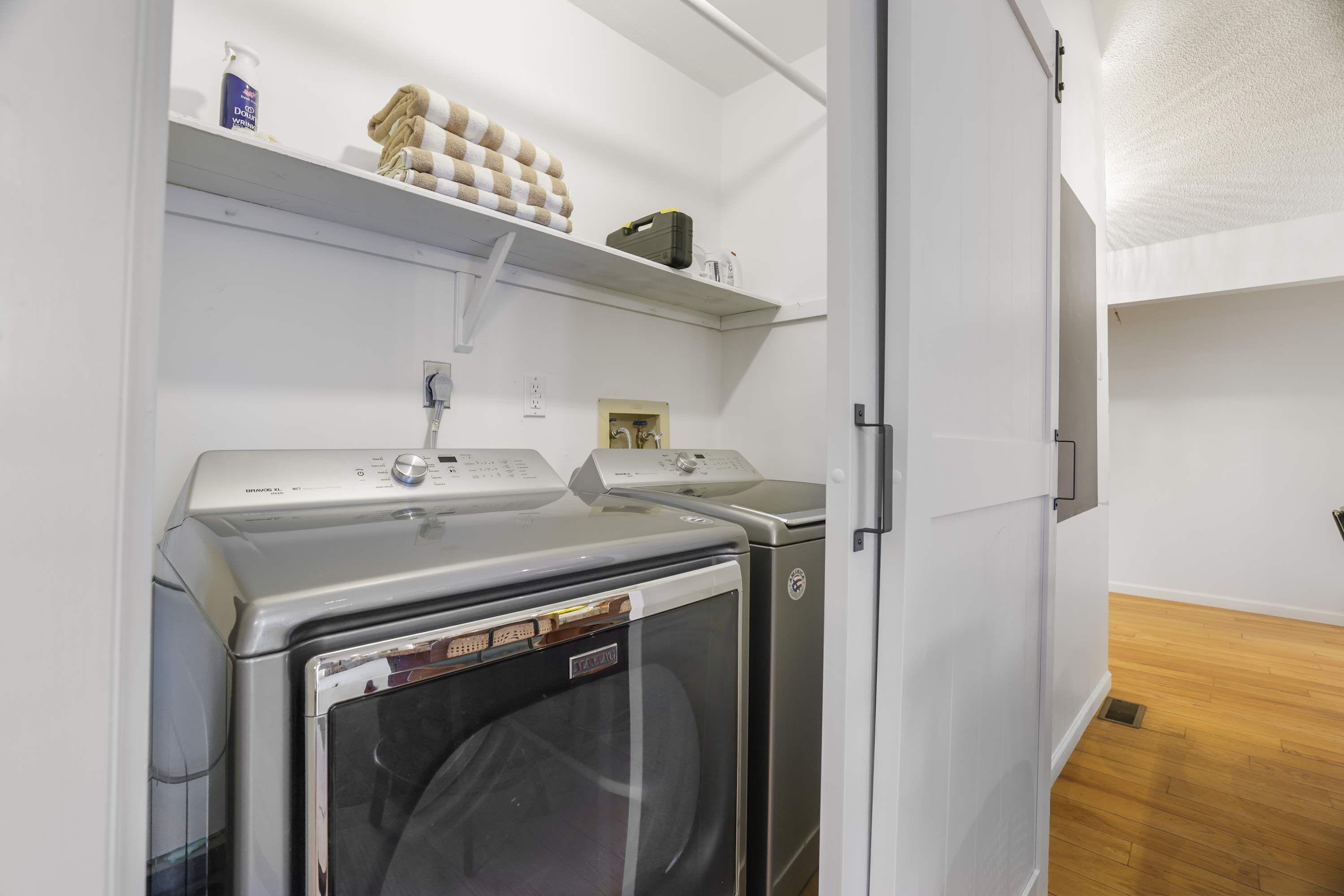 A laundry room with two front-loading washing machines, a shelf with towels, and a white door.