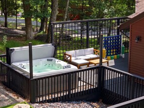 A hot tub area with a wooden deck, a white sofa, and a wooden table. - The Ridge at Penn Estates A 4BR Pocono Retreat (East Stroudsburg)