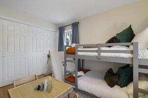 Quarto com beliche, mesa de madeira, porta branca e janela com cortinas.