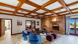 A spacious living room with a high wooden ceiling, a brick fireplace, and a large window with a view. - Lake Mathews Estate Indoor Pool Pickleball Beach Volleyball (Perris)