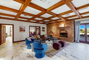 A spacious living room with a high wooden ceiling, a brick fireplace, and a large window with a view. - Lake Mathews Estate Indoor Pool Pickleball Beach Volleyball (Perris)