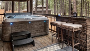 A hot tub with stone exterior, two black chairs, and a wicker bar with cushions. - NEW Black Butte Ranch Sauna Hot Tub Kids Playroom (Sisters)