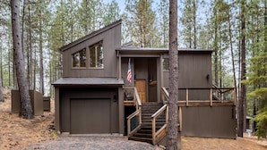 A two-story cabin with a garage, a wooden staircase, and an American flag. - NEW Black Butte Ranch Sauna Hot Tub Kids Playroom (Sisters)