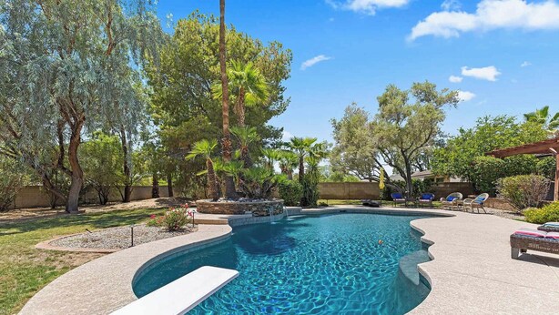 A swimming pool with a curved edge, surrounded by trees and a patio area with lounge chairs. - Waz-4901 E Sunnyside Dr (Scottsdale)