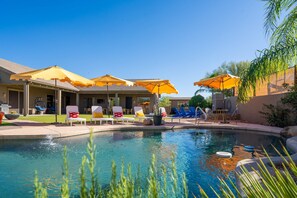A pool area with lounge chairs and umbrellas, a clear sky, and a building with a tiled roof. - Suncrest Pool Pickleball Theater (Scottsdale)