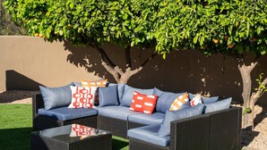 Ein Sitzbereich im Freien mit einem Ecksofa und einem Couchtisch, umgeben von Kunstgrün und einem Baum.