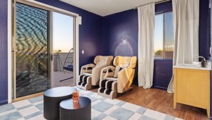 Ein Zimmer mit Massagesessel, einem kleinen Tisch mit einer Dekoration und Blick ins Freie durch eine Schiebetür.