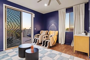 Ein Zimmer mit Massagesessel, einem kleinen Tisch mit einer Dekoration und Blick ins Freie durch eine Schiebetür.