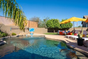 A clear swimming pool with a blue water feature, surrounded by a patio area with outdoor furniture and a cactus plant. - Suncrest Pool Pickleball Theater (Scottsdale)