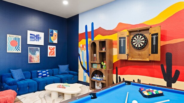 Ein Raum mit Billardtisch, blauem Sofa und farbenfroher Wandmalerei.
