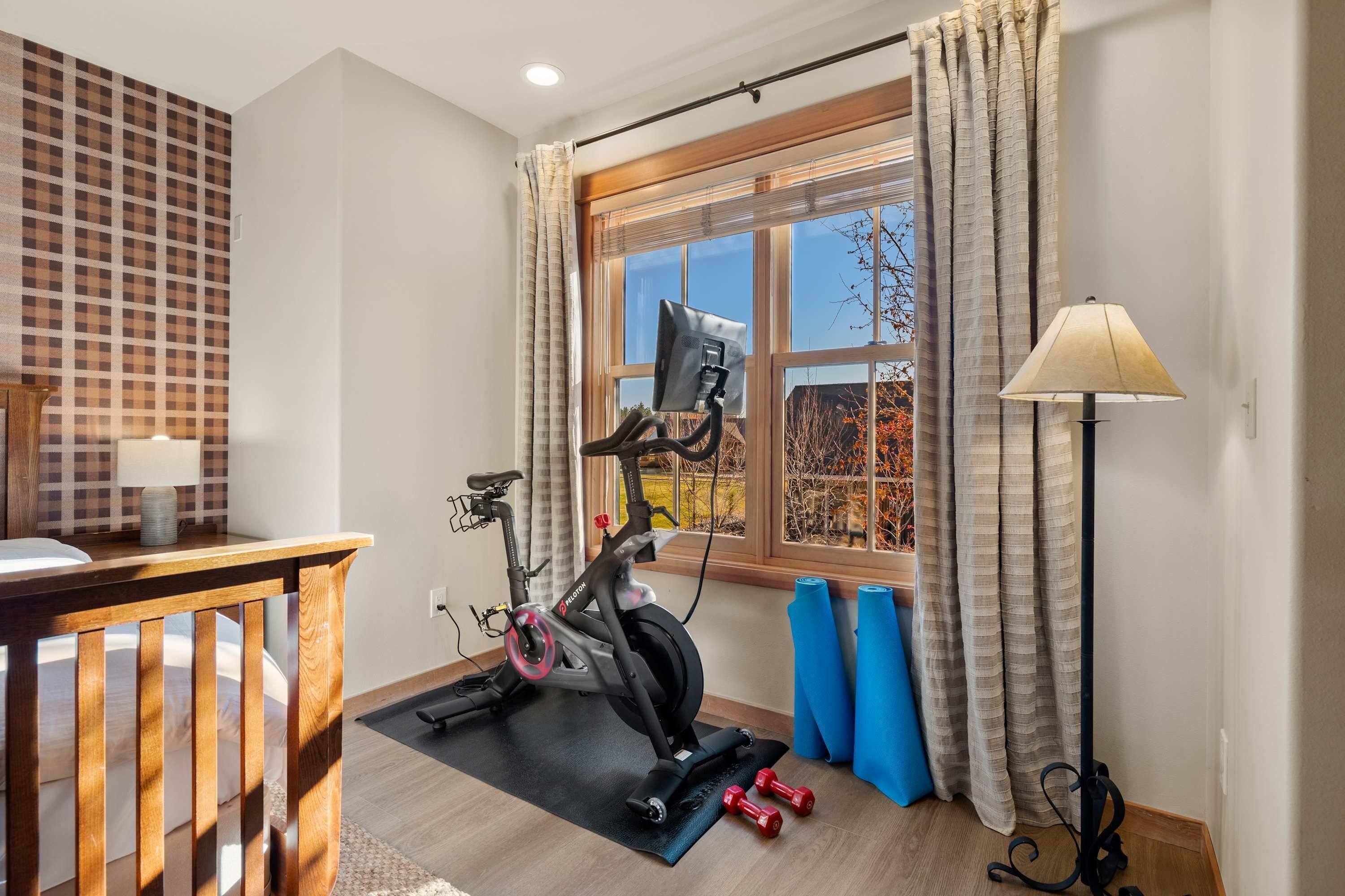 A room with a stationary bike, exercise mats, a desk, and a lamp.