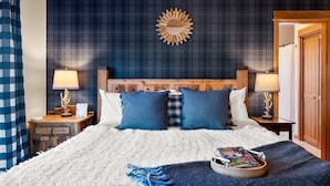Ein Bett mit Holz-Kopfteil, zwei Nachttische mit Lampen, eine Wand mit Karomuster und eine Holztür.