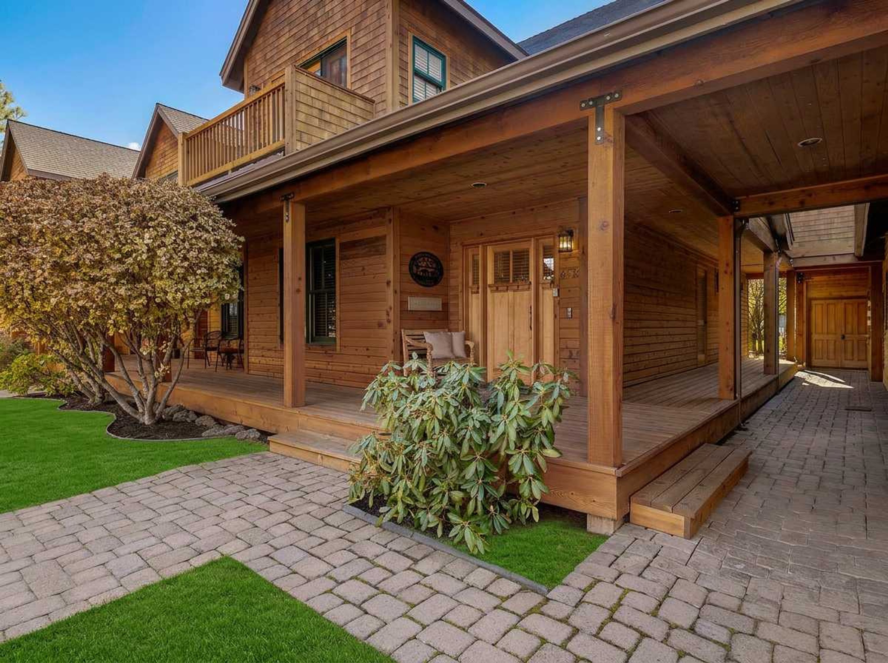 Una cabaña de madera con un porche cubierto, un pequeño jardín y un sendero pavimentado.