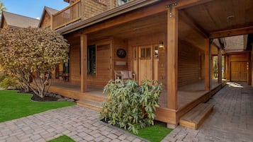 Una cabaña de madera con un porche cubierto, un pequeño jardín y un sendero pavimentado.