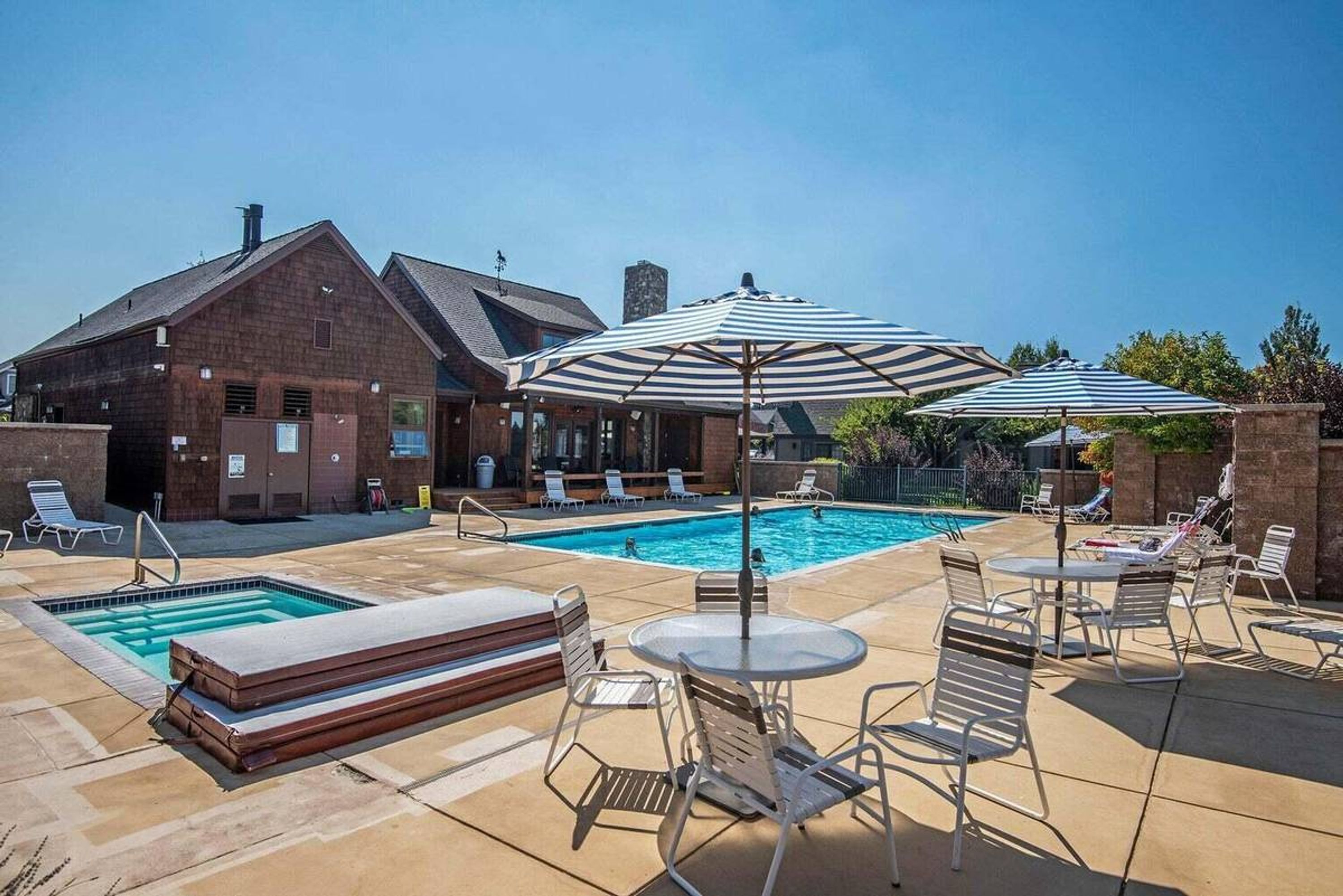 A pool area with lounge chairs, umbrellas, and a brick building in the background.