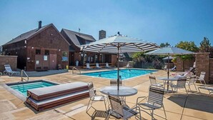 Ein Poolbereich mit Liegestühlen, Sonnenschirmen und einem Backsteinhaus im Hintergrund.