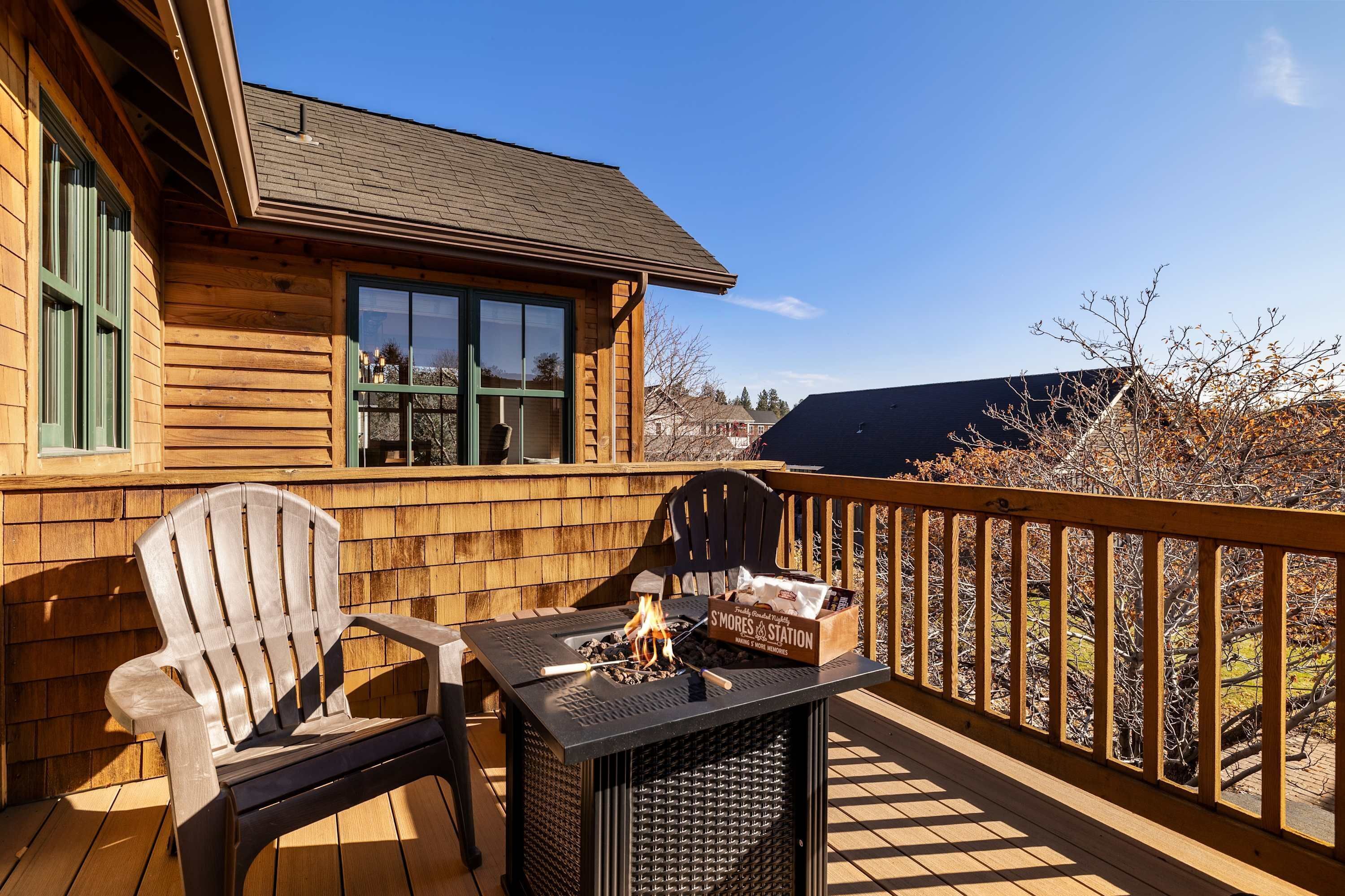 A wooden deck with a table and two chairs, a box of S'mores, and a fire pit.