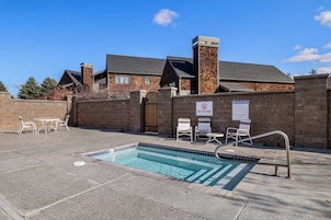 Zona de piscina con hidromasaje, sillas de descanso y un muro de ladrillo.