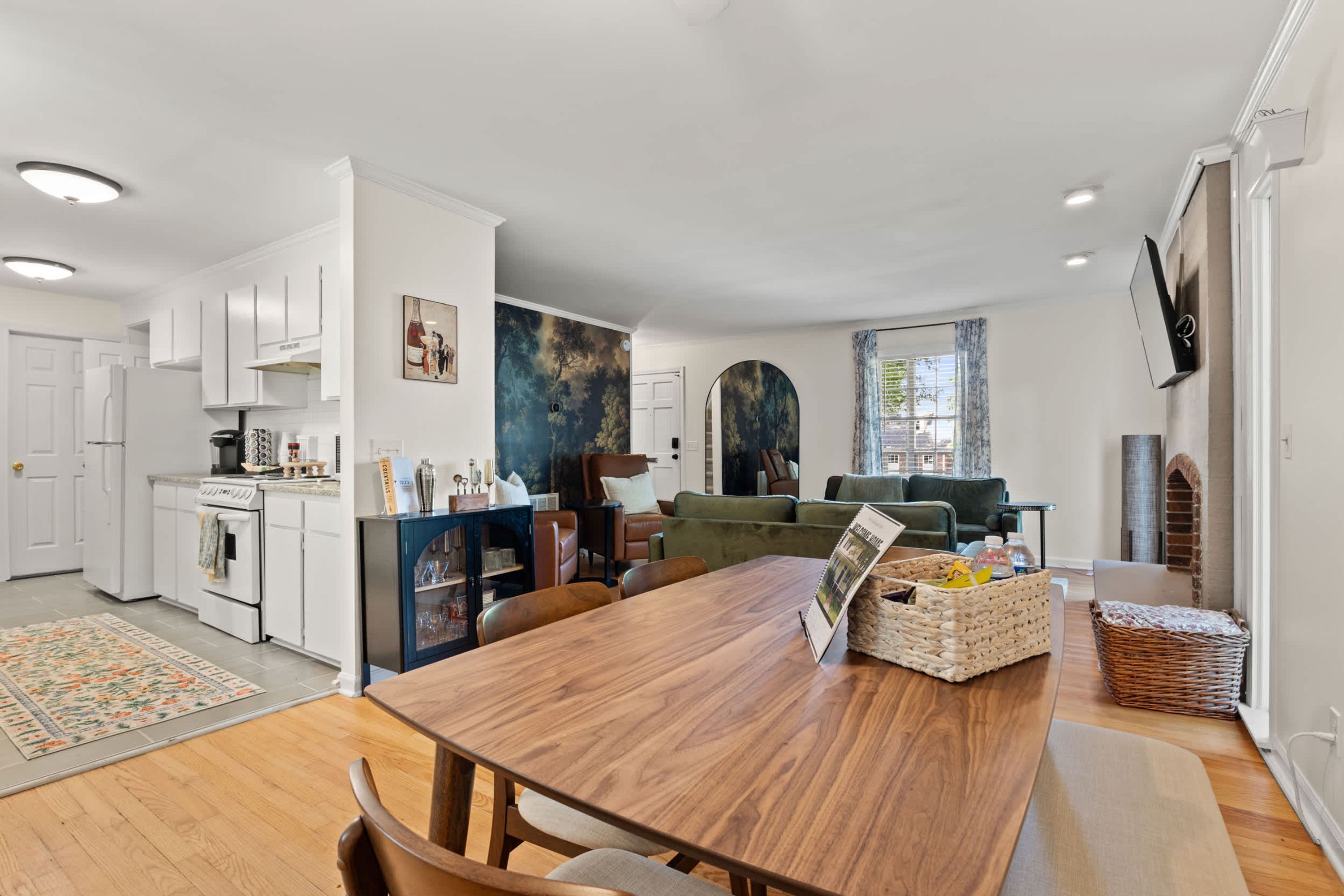 Una cocina moderna con gabinetes blancos, un comedor con mesa de madera y una sala de estar con sofá verde.