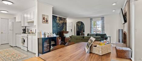 Una cocina moderna con gabinetes blancos, un comedor con mesa de madera y una sala de estar con sofá verde.