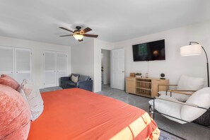 Un dormitorio con una cama, un escritorio, una silla, un televisor y un ventilador de techo.