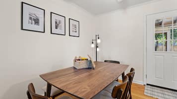 A dining room with a wooden table, four chairs, and a basket of snacks. There are three framed pictures on the wall.