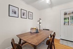 A dining room with a wooden table, four chairs, and a basket of snacks. There are three framed pictures on the wall. - Near USC Downtown Fire Pit Dog Friendly (Columbia)