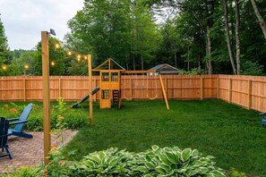 A backyard with a wooden playhouse, a swing set, and a brick patio area. - Mountain Getaway Outdoor Games Sauna Hot tub (North Conway)