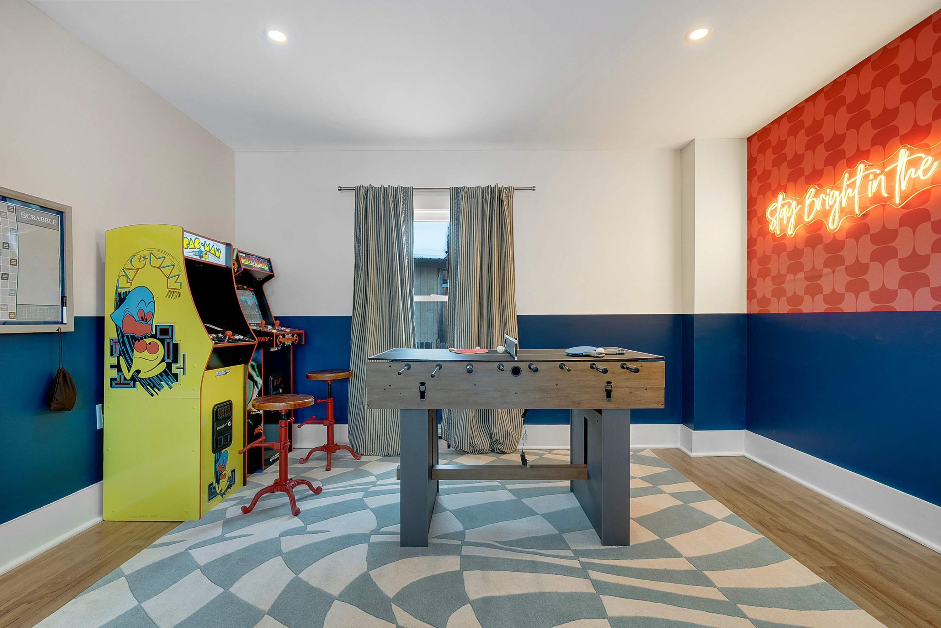 A room with a foosball table, arcade games, and a neon sign.