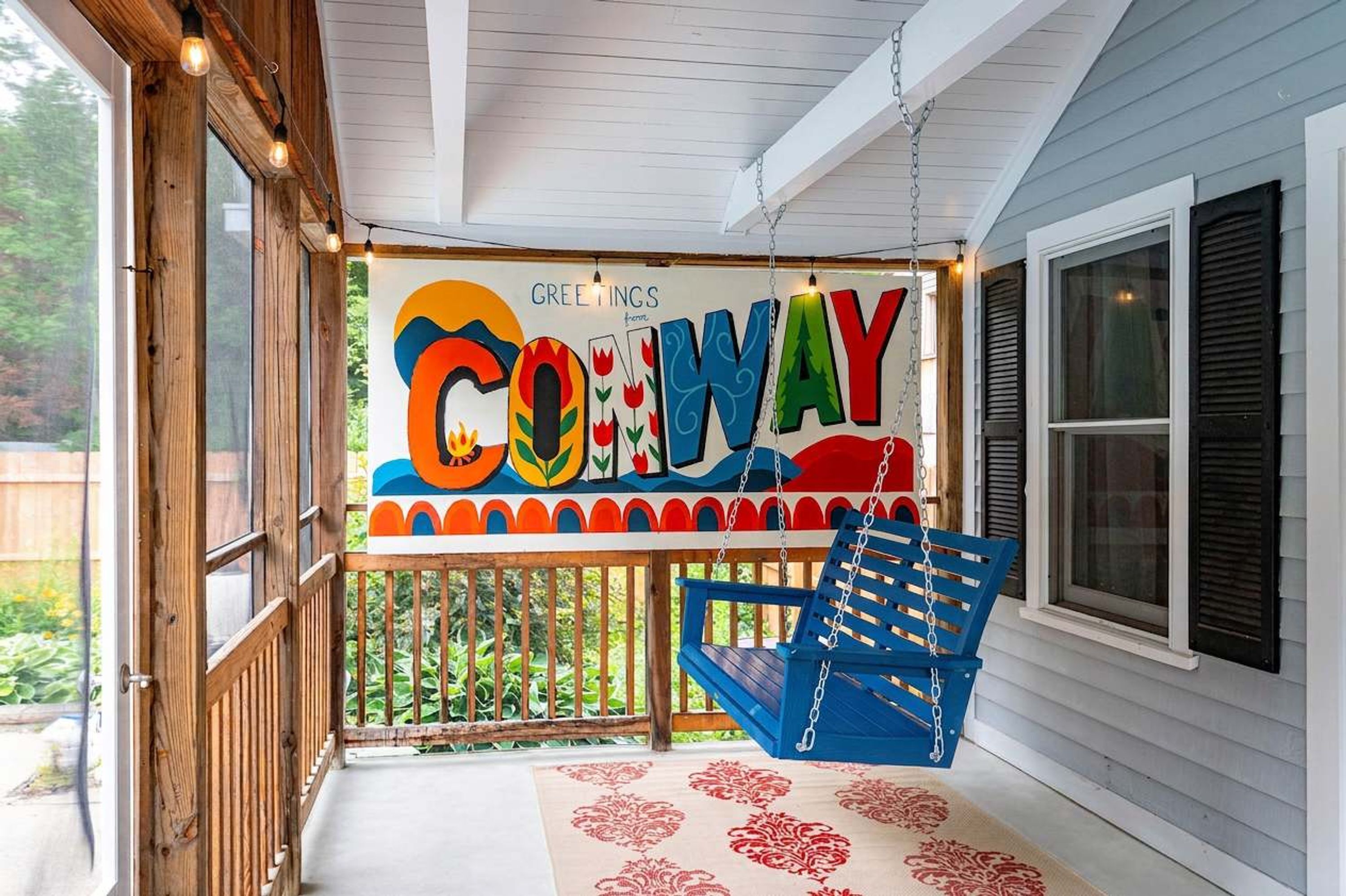 A porch with a swing chair, a decorative sign, and a view of greenery.