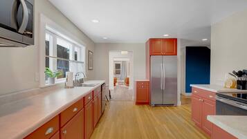 A modern kitchen with stainless steel appliances, wooden flooring, and a view to the living area.