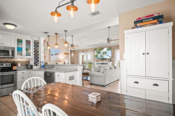 A spacious kitchen with white cabinetry, a wooden dining table, and pendant lighting. - Coastal Casa-ocean Views Family Friendly 5BR (Port Aransas)