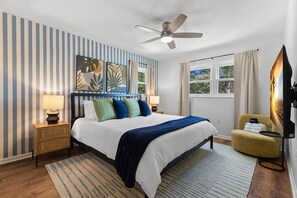 A hotel room with a bed, bedside lamps, a ceiling fan, a window with curtains, a television, and a chair. - 4 Minutes to Beach Pool Hot Tub Game Room (Seminole)