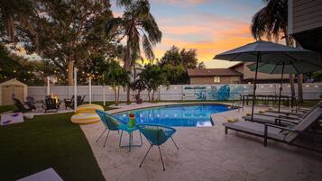 A backyard with a swimming pool, lounge chairs, and a fire pit.