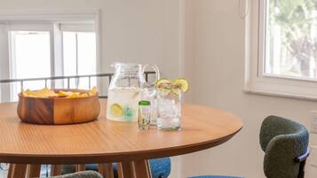 A wooden table with a bowl of chips, a pitcher of water with lime slices, and a glass with a straw.