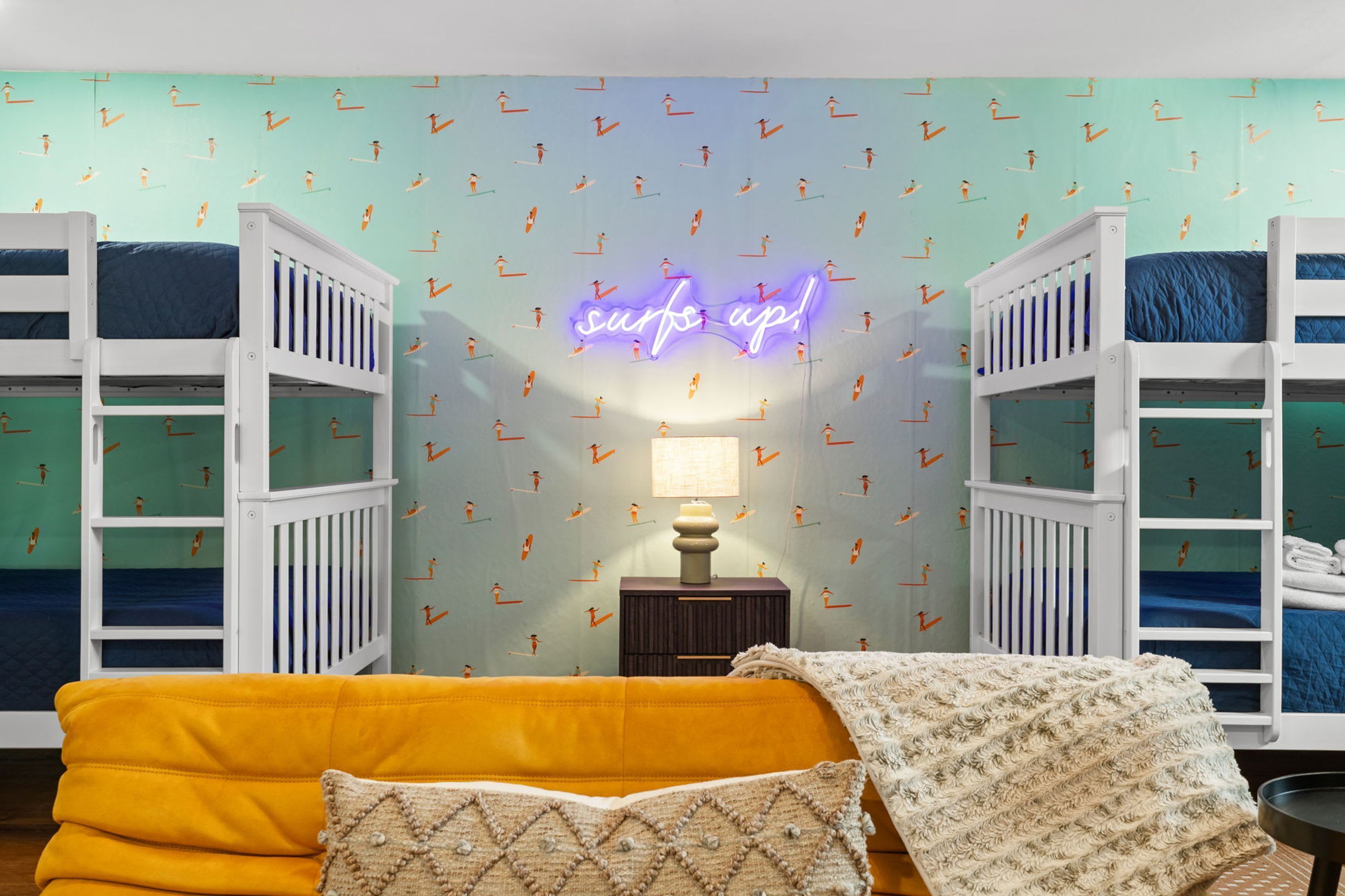 A room with bunk beds, a neon sign, a lamp, and a sofa.