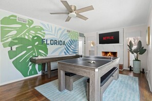 Ein Zimmer mit Tischtennisplatte, Kamin, Wandfernseher und Deckenventilator.