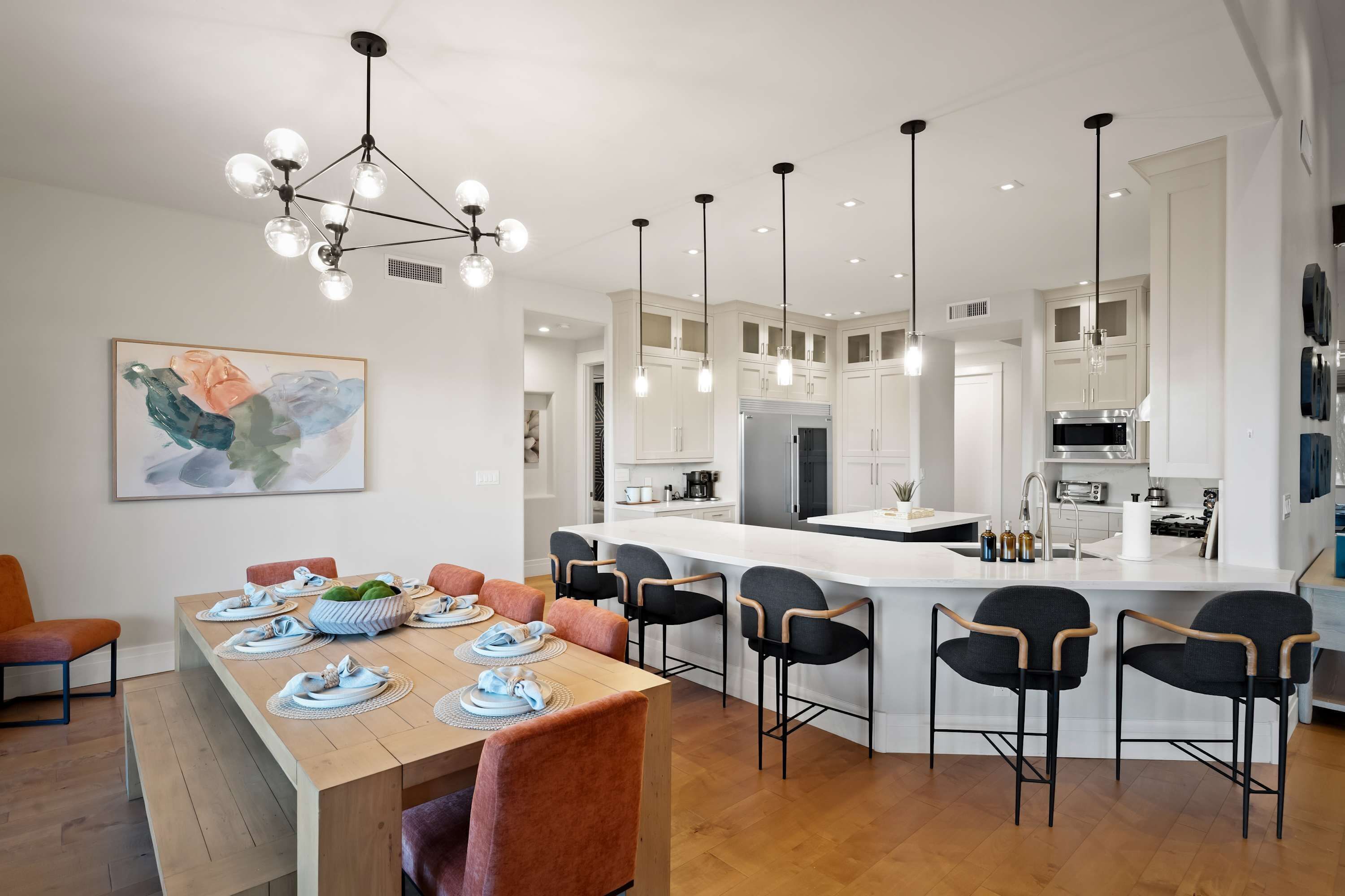 A modern kitchen with a central island, pendant lighting, and a dining area with a wooden table and chairs.