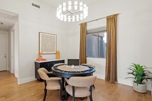 A dining area with a round table, four chairs, a chandelier, a framed picture, a bottle, and a window with curtains. - The Good Life Oasis Luxury 5BR Home Sleeps 16 (Glendale)