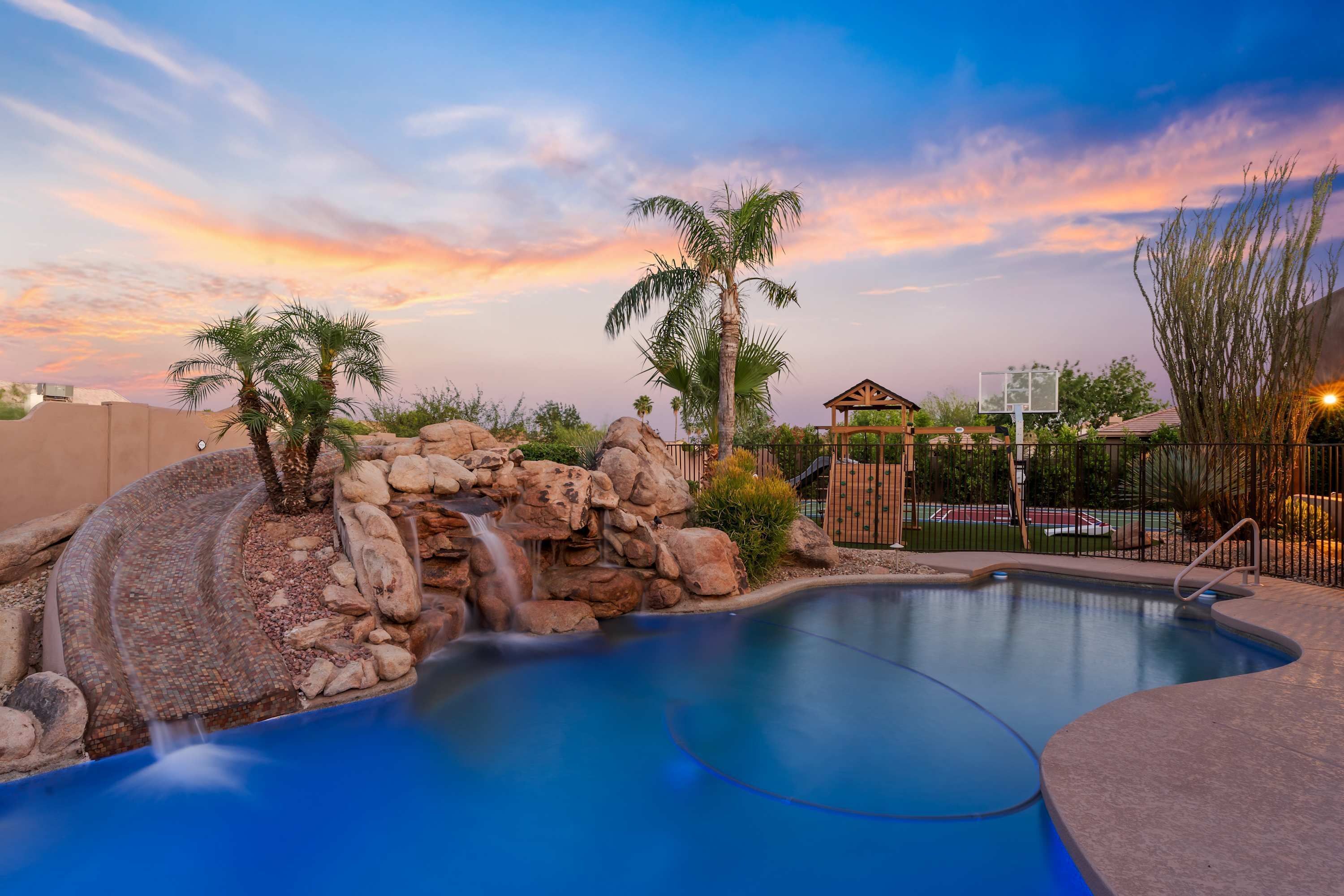 A swimming pool with a waterfall feature, surrounded by rocks and palm trees.